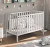 A baby crib in a nursery setting with decorative elements on the wall and a rug on the floor. Anteprima dell’immagine prodotto