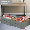 Two storage boxes filled with items, placed on a floor in front of a desk. Produktbild-Vorschau