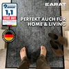 A person's feet are standing on a doormat in front of a doorway, with a pair of slippers placed on the mat. Náhled obrázku produktu