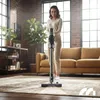 A woman is vacuuming a rug in a living room with a cordless vacuum cleaner. Podgląd zdjęcia produktu