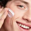 A close-up shot of a person applying cream to their face. Produktbild-Vorschau