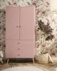 A pink wardrobe with three drawers stands against a floral wallpaper. Produktbild-Vorschau