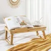 A bamboo laptop table with an open book and a cup of coffee on a bed. Produktbild-Vorschau