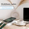 A desk scene with a phone charging wirelessly, a cup of coffee, a laptop, and a vase with dried flowers. Produktbild-Vorschau