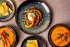 A top-down view of several plates of food, including roasted pumpkin, carrots, and a crepe with orange slices. Náhľad obrázku produktu