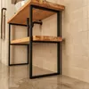 A close-up shot of a wooden and black metal washstand frame against a tiled wall. Produktbild-Vorschau