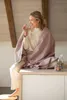 A woman wrapped in a blanket drinks water while sitting on a counter. Produktbild-Vorschau