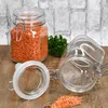 Two glass jars with clamp lids, one filled with red lentils and the other empty, sit on a wooden surface with a brick wall in the background. A sprig of parsley is also visible. Náhled obrázku produktu