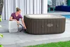 A woman is connecting a pump to an inflatable hot tub next to a swimming pool. Produktbild-Vorschau