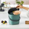 A person is placing coffee pods into a teal compost bin on a kitchen counter. Produktbild-Vorschau