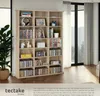 A well-lit interior scene featuring a wooden bookshelf filled with CDs, DVDs, and decorative items, with large windows and curtains in the background. Náhled obrázku produktu