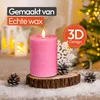A pink LED candle with a flame sits on a wooden slice, surrounded by snow and pinecones, with a Christmas tree and lanterns in the background. Produktbild-Vorschau