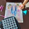 A person's hand is shown working on a diamond painting kit, with various accessories laid out on a wooden table. Produktbild-Vorschau