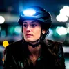 A woman wearing a black helmet with a bright light on the front, at night. Produktbild-Vorschau