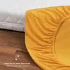 A close-up of a yellow fitted sheet draped over a mattress, with a portion of the mattress visible in the background. Anteprima dell’immagine prodotto