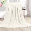 A cream-colored blanket is draped over a piece of furniture, with a window and a brick wall in the background. Produktbild-Vorschau