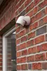A white LED outdoor light with a motion sensor is mounted on a red brick wall next to a window. Produktbild-Vorschau