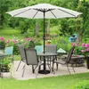 A patio set with a large umbrella, table, and chairs, surrounded by a garden with pink flowers. Produktbild-Vorschau