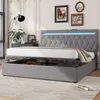 A grey upholstered bed with storage is shown in a bedroom setting with a lamp and artwork on the wall. Produktbild-Vorschau