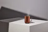 A bronze mug with steam rising from it, placed on a white cube against a gray background with dramatic shadows. Voir les images du produit