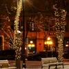 A street scene at night, decorated with string lights on trees and buildings, with snow on the ground and benches. Voir les images du produit