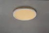 A round, white LED ceiling light with a wood-effect trim is mounted on a textured gray ceiling. Produktbild-Vorschau
