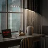 A modern desk setup with a laptop, books, a vase with branches, and a floor lamp, next to a window with a city view. Anteprima dell’immagine prodotto