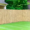 A natural reed fence in a garden setting, with a lawn in the foreground and trees and a house in the background. Produktbild-Vorschau
