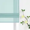 A close-up view of a light green linen Roman blind with a decorative branch with light yellow flowers and green leaves to the right. Produktbild-Vorschau