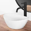 A white oval basin sink with a black faucet on a wooden countertop, with a round mirror in the background. Náhled obrázku produktu