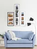 A light blue sofa with a white throw blanket is placed in front of a wall with several framed pictures. A floor lamp with two black shades stands to the right of the sofa. Podgląd zdjęcia produktu