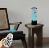 A lava lamp with artificial fish is placed on a side table next to a chair, with a remote control in the foreground. Produktbild-Vorschau