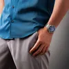 A man's torso and arm wearing a blue shirt, gray pants, and a silver watch. Anteprima dell’immagine prodotto