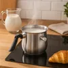 A stainless steel milk pot with milk boiling on an induction hob, next to a glass jug of milk and a croissant. Produktbild-Vorschau
