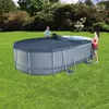 Two people are covering an oval above-ground swimming pool with a dark blue cover on a sunny day in a grassy backyard. Podgląd zdjęcia produktu