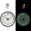 A split image showing a glowing wall clock in both daytime and nighttime conditions. Voir les images du produit