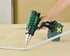 A hand holding a cordless heat gun, aiming it at a white pipe on a wooden surface. Produktbild-Vorschau