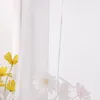 A close-up of sheer white curtains with yellow and white flowers in the foreground. Produktbild-Vorschau
