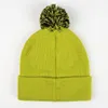A close-up view of the back of a green knitted hat with a black and yellow pom-pom on top. Podgląd zdjęcia produktu
