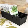 A black organizer tray holding several packets of seeds, with bay leaves scattered around the base. Anteprima dell’immagine prodotto