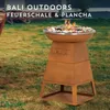 A rusty metal fire pit and grill with food cooking on it, set up on a grassy lawn. Produktbild-Vorschau