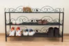 A three-tiered black metal shoe rack with various shoes on each shelf. The background is a plain, lightly textured wall and a wooden floor. Produktbild-Vorschau