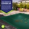 A green pool cover is spread out on a wooden deck, with some leaves on it. In the background, there is a table with chairs and a house. Podgląd zdjęcia produktu