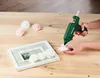 A person is using a hot glue gun to attach a pink rose to a picture frame. Produktbild-Vorschau