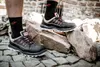 A person wearing black safety shoes and socks is standing on cobblestones and rocks. Voir les images du produit