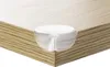 A close-up shot of a transparent corner protector on the edge of a wooden table. Produktbild-Vorschau