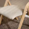A close-up view of a beige upholstered folding chair with light wood legs, resting on a brown carpet. Náhľad obrázku produktu