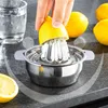 A hand is using a stainless steel citrus juicer to extract juice from a lemon, with other lemons and a glass of water in the background. Produktbild-Vorschau