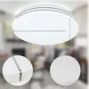 A close-up view of a modern, round LED ceiling light with a white finish, set against a blurred background of a living room interior. Two magnified circular insets show details of the light's edge and surface texture. Anteprima dell’immagine prodotto