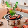 Two people toasting with beer bottles over a BBQ grill with food on it. Náhled obrázku produktu